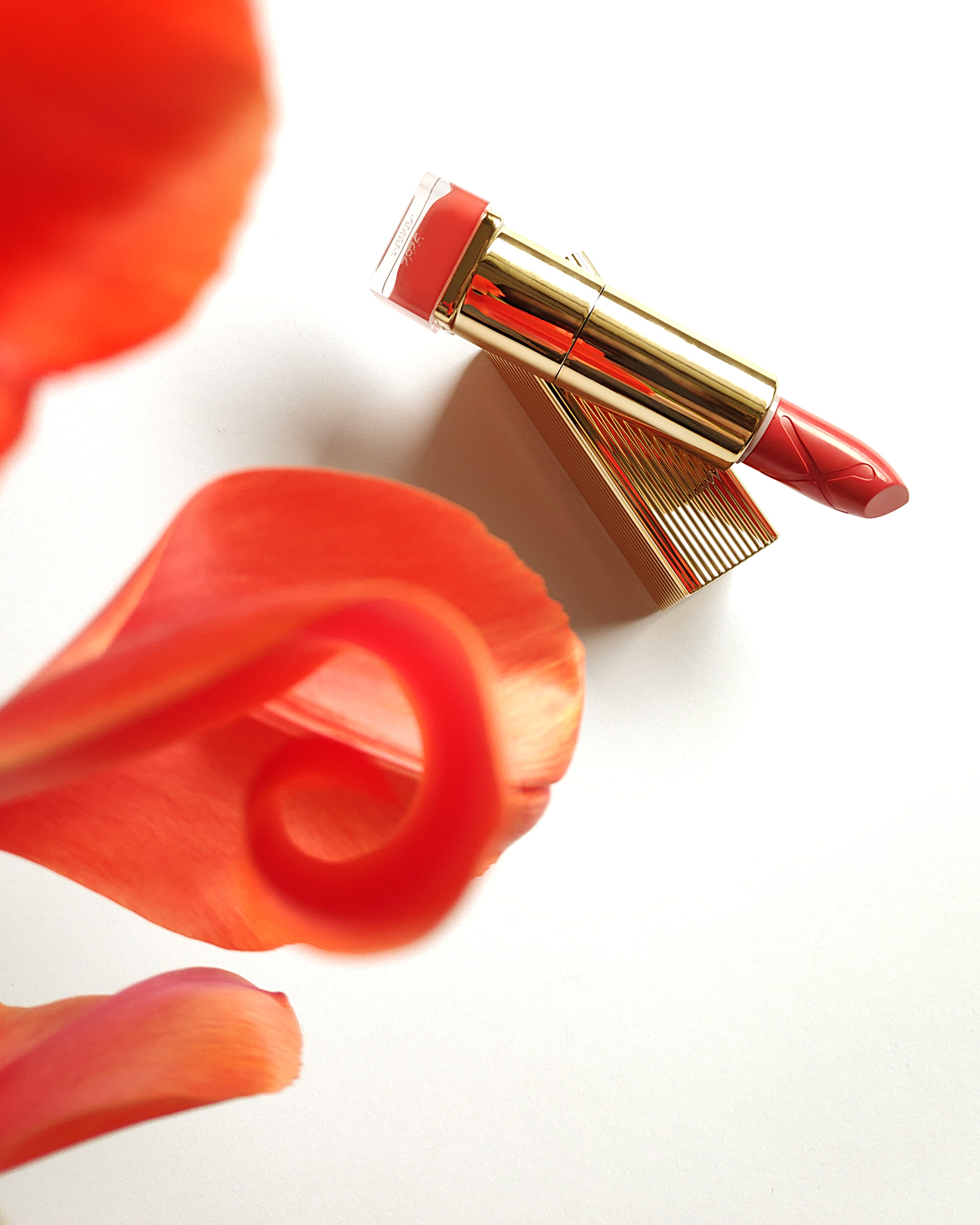 Max Factor Colour Elixir Lipstick in 050 Pink Brandy, a vibrant coral lipstick with open cap, and a bright red tulip next to it on a white background.