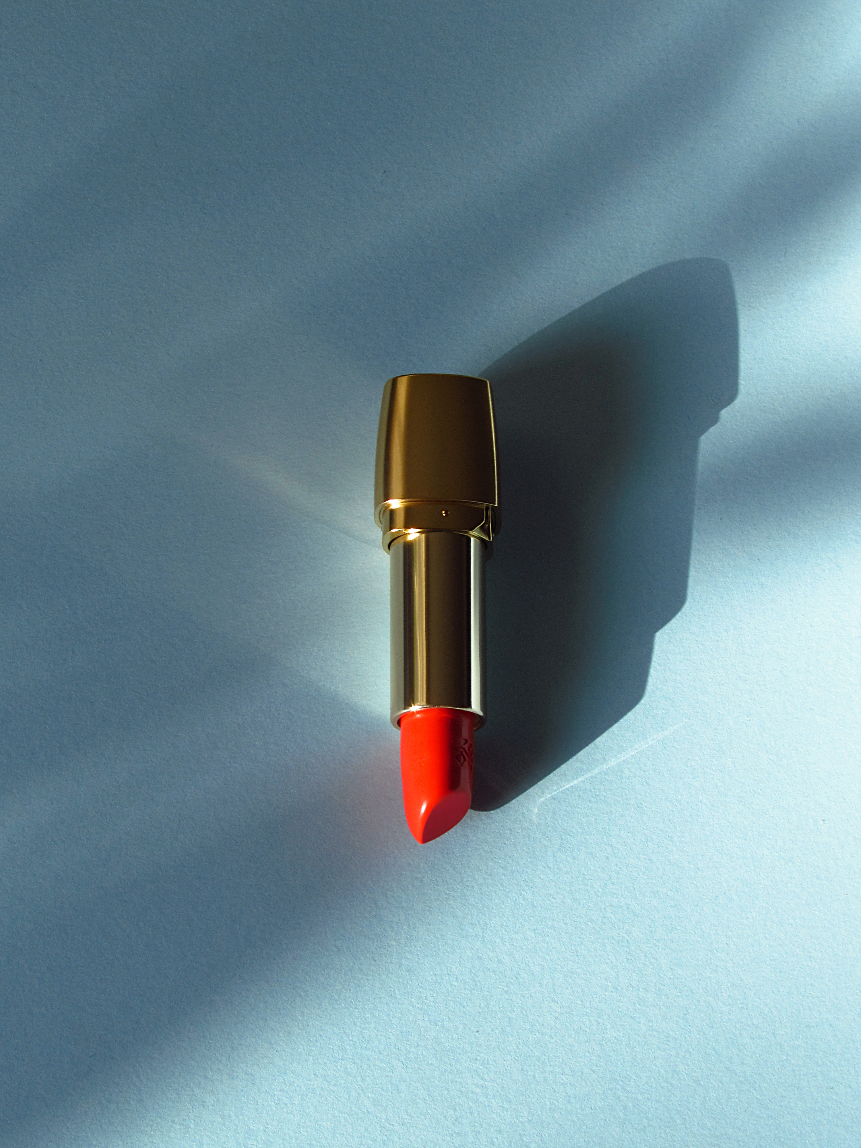 Deborah Milano Rossetto Milano Red Lipstick in No. 11 under the afternoon light on a blue background.