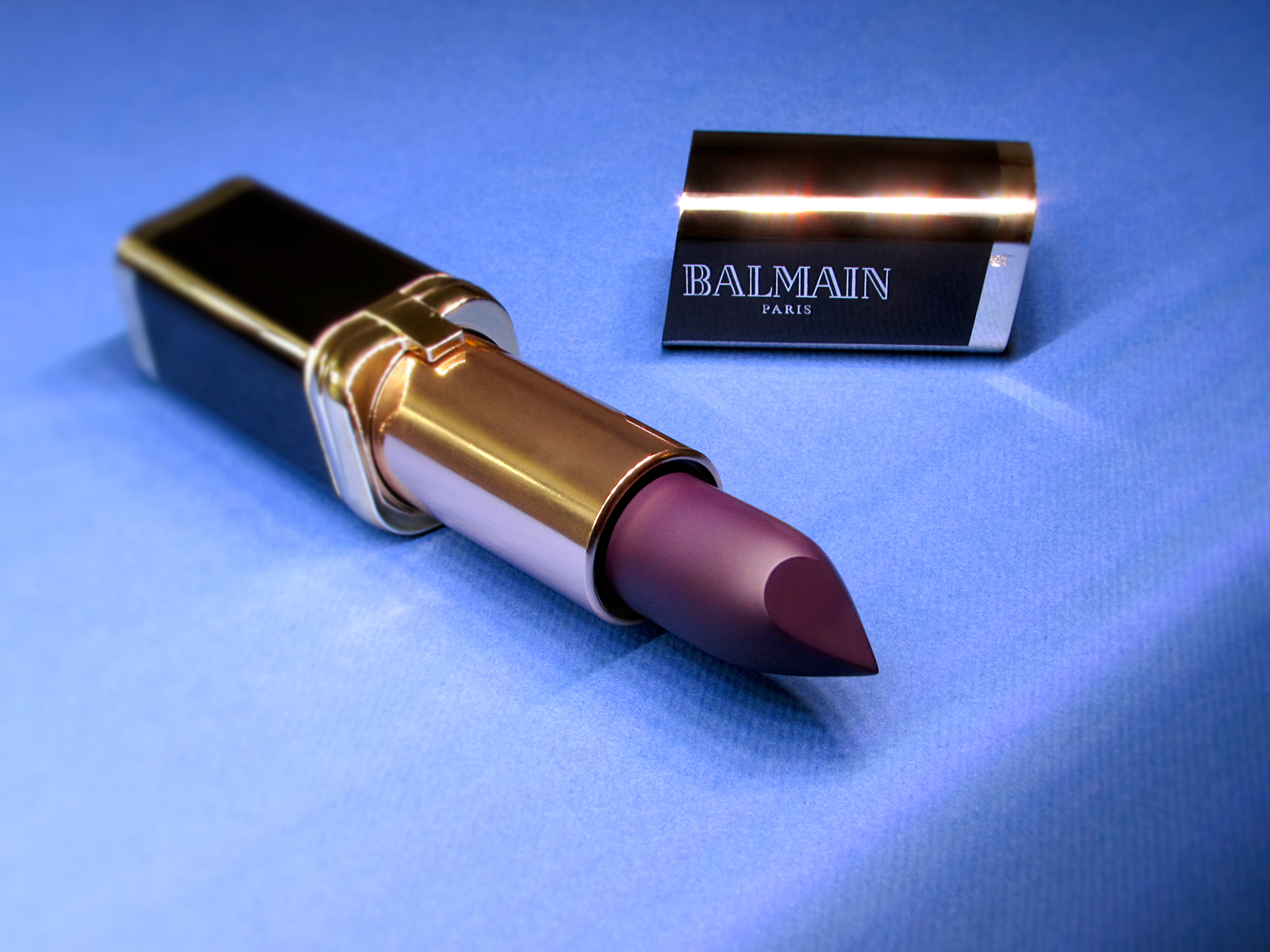 L’Oréal Paris x Balmain Color Riche limited edition purple lipstick in 468 Liberation opened on a blue background.